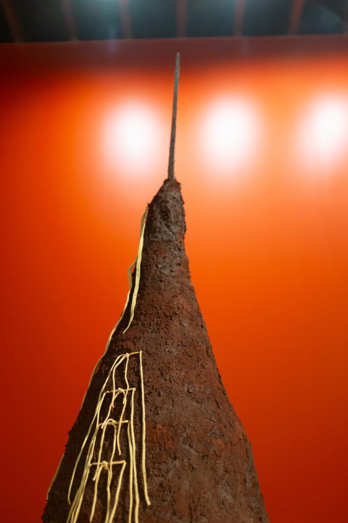 Peak of a sculpture, coming to a point with a long protrusion from its tip. Strings of leather are tied from its side.