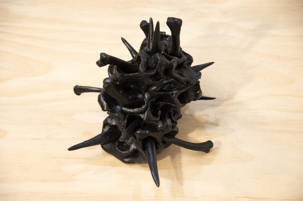 Shiny black ceramic sculpture with bones protruding from orifices in blob shape