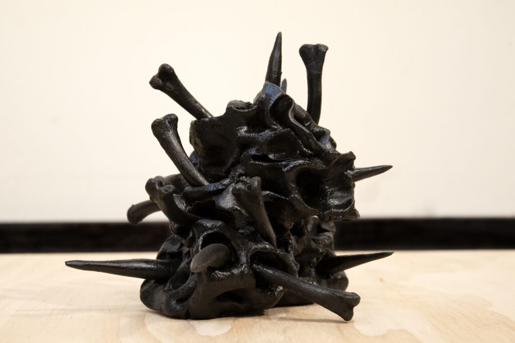 Shiny black ceramic sculpture with bones protruding from orifices in blob shape